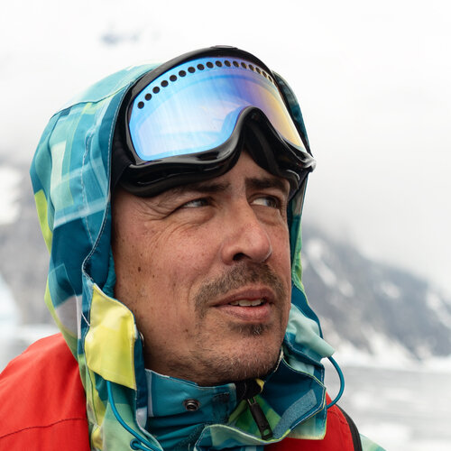 A middle-aged white man wearing snow goggles against a snowy background