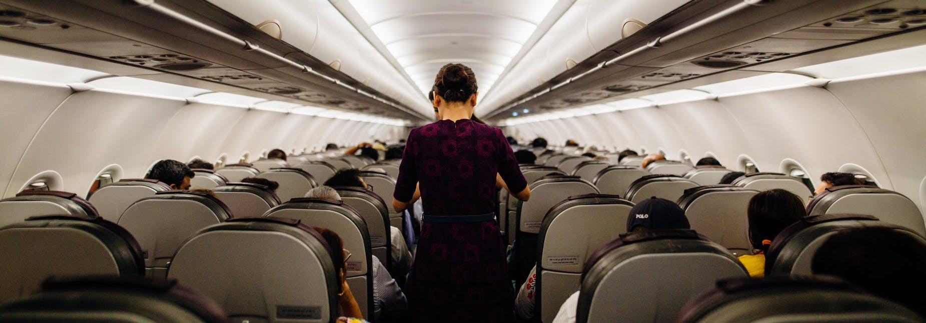 A flight attendant standing in the aisle of a relatively full airplane