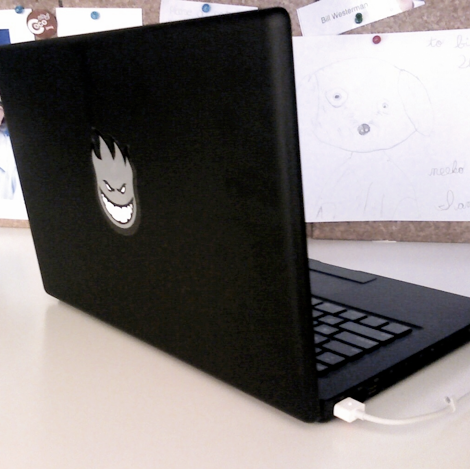 Black MacBook laptop from 2006 with a grinning Spitfire skateboarding sticker covering the Apple logo