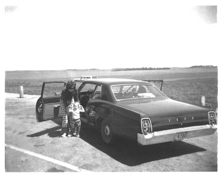 My mom and me next to an old Ford near a lake