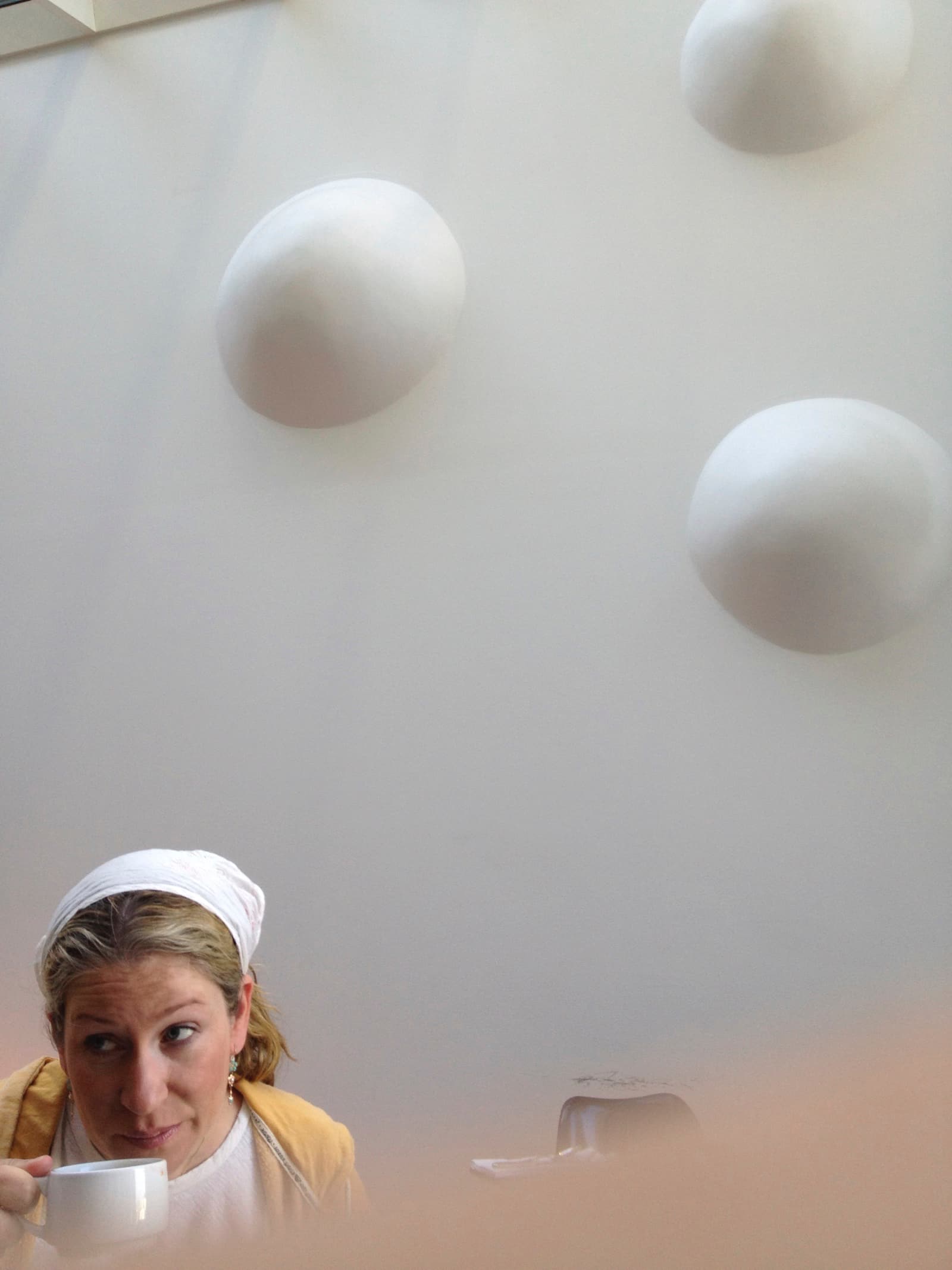 A woman drinking coffee in front of a wall covered with giant hemispherical bumps