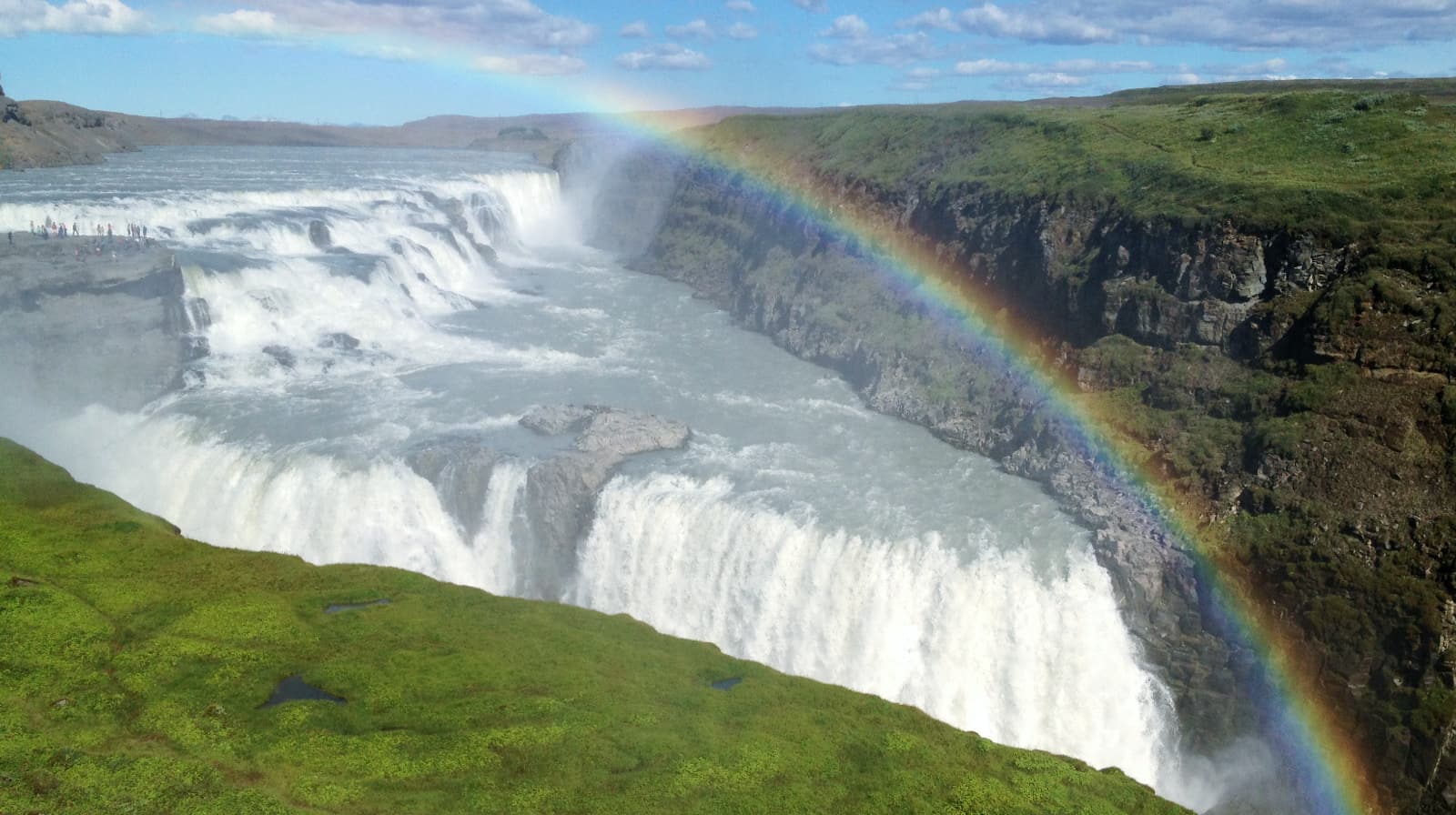 Large horizontally spread out waterfall with a rainbow
