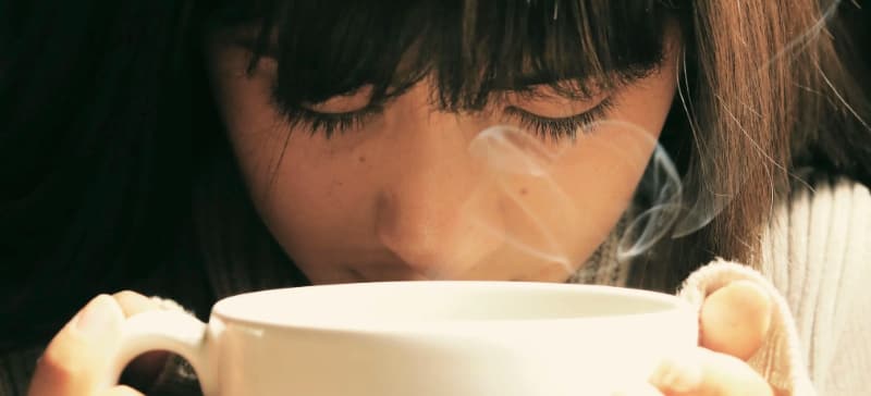 A woman smelling a coffee cup with steam coming out of it