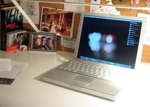 A PowerBook 12 sitting on a desk, with various papers and photos in the background