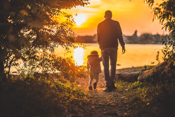 A dad and a child walking near a lake at sunset