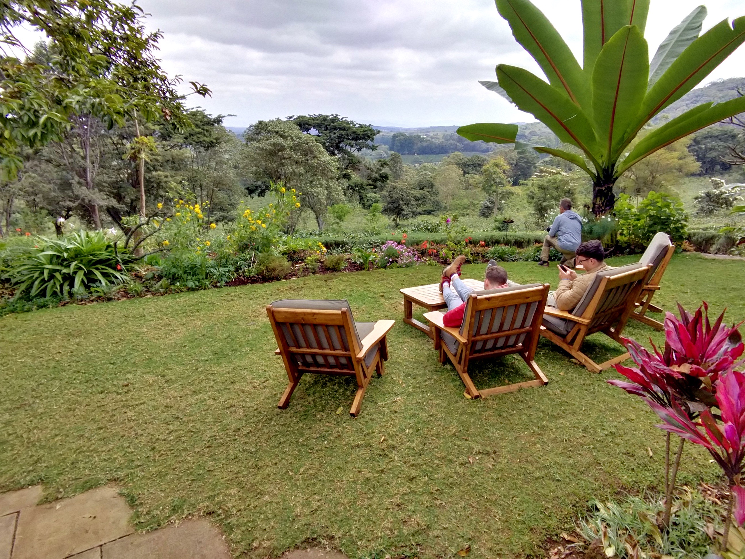 Three lawn chairs and two young men in a lush environment overlooking the hills